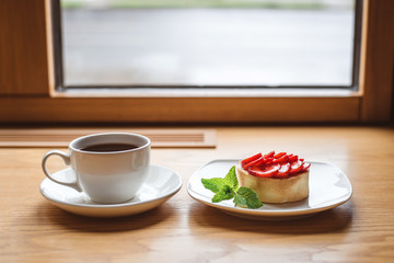 Strawberry tartlet and a cup of tea on wooden table near the window.