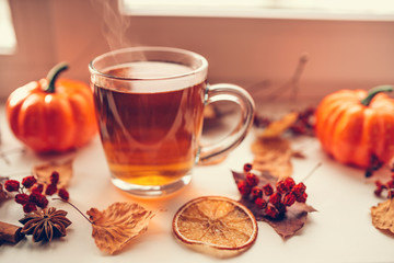 Hot steaming Cup of tea with autumn leaves, pumpkins and spices on the windowsill. Autumn mood.