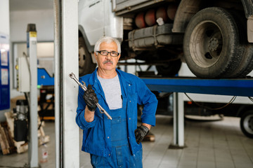 Serious grey-haired man in workwear standing in workshop or hangar