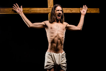 shirtless man crucified on wooden cross screaming isolated on black
