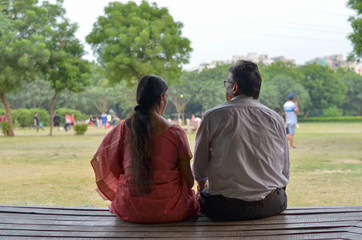 Senior citizen couple shot from back relaxing, talking, sitting in a park in Delhi, India. Concept...