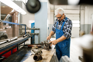 Mature professional repairman of car maintenance service standing by workbench