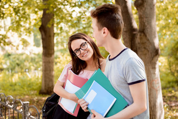 Female student in love looking at a handsome classmate in the park, flirting with him and...