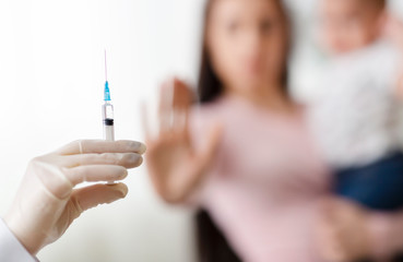 Mother holding baby and rejecting doctor with syringe