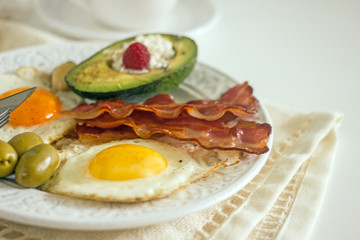 Keto Diet LCHF Keto breakfast. Fried eggs with bacon, avocado, cream cheese, nuts, olives on a white plate on a light background. Low carb diet concept. high fat diet. Keto bacon and eggs 