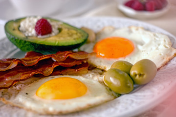 Keto Diet LCHF Keto breakfast. Fried eggs with bacon, avocado, cream cheese, nuts, olives and coffee on a white plate on a light background. Low carb diet concept. high fat diet. Keto bacon and eggs 