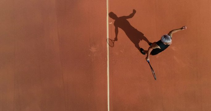 A mixed race platinum hared tennis player throws the ball high into the air, serves and celebrates serving an 'Ace'.