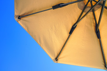 Looking up towards a blue sky under a yellow sun umbrella