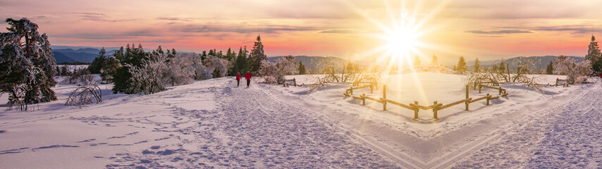 Panorama von Winterlandschaft mit Schnee mit Menschen die während eines Sonnenuntergangs spazieren...