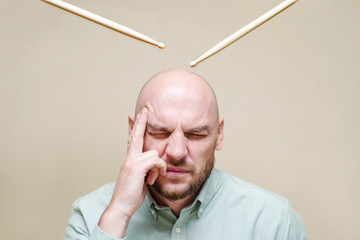 Portrait of a man with closed eyes compresses temporal area hands and drumsticks over his head....