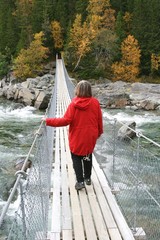 Middle aged woman walking on a suspension bridge over a stream in autumn