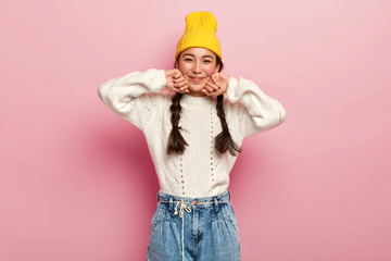Pretty mixed race female dressed in fashionable yellow hat, white sweater and jeans, has...
