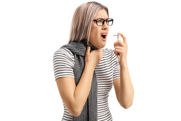 Young woman suffering from an allergy spraying a medication and holding her throat