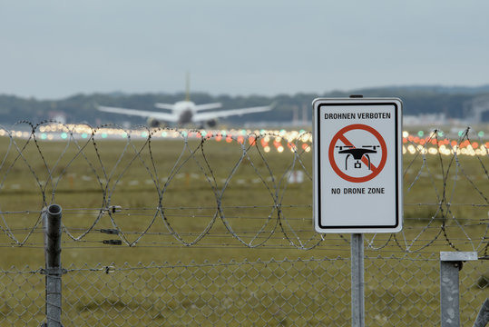Prohibition sign at German airport "Dronen Verboten" with aircraft ab runway in the background