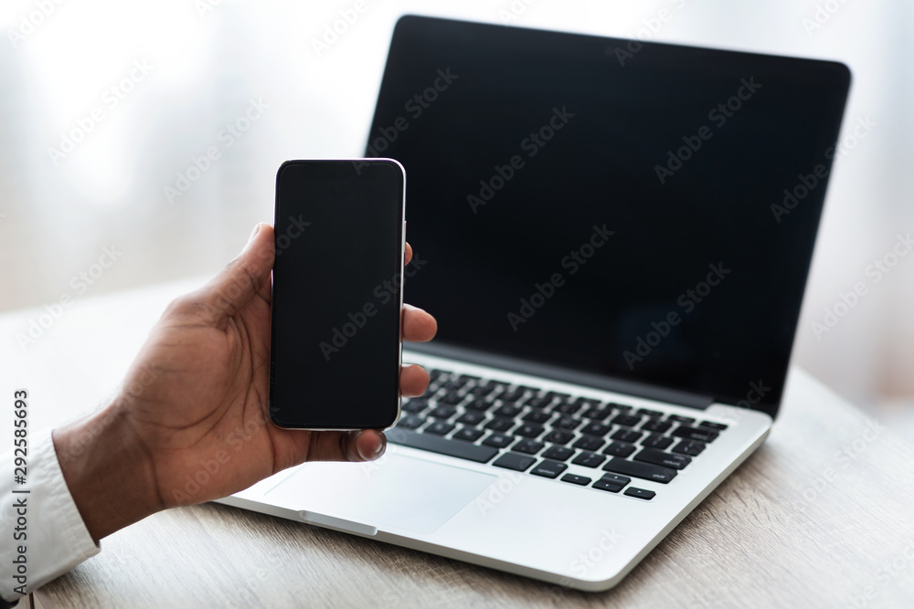 Wall mural black man holding smartphone with blank screen, while using laptop