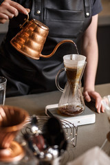 Fototapeta na wymiar Professional barista preparing coffee using chemex pour over coffee maker and drip kettle. Young woman making coffee. Alternative ways of brewing coffee. Coffee shop concept.