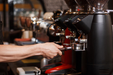 Professional coffee grinder grinding fresh roasted coffee beans. Barista holding bottomless portafilter holder with ground coffee. Brewing coffee. Coffee shop concept.