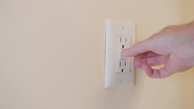 Close up of male hand resetting tripped GFI electricity receptacle. Residential ground fault interrupter electric socket plug and wall plate.