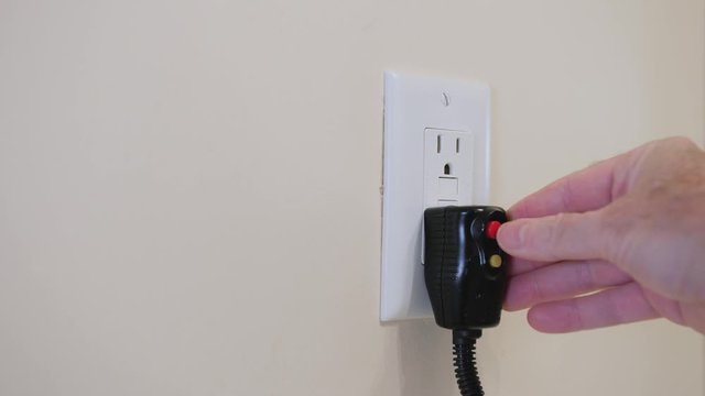 Close up of male hand inserting cord with GFI plug into electricity receptacle. Residential ground fault interrupter electric socket plug and wall plate.