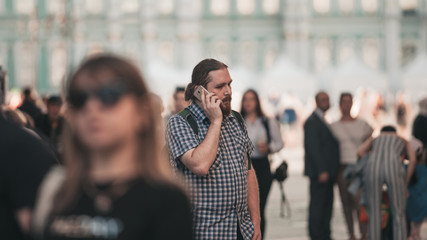 guy in a crowd on a big city street. A young bearded man in the city uses a mobile phone