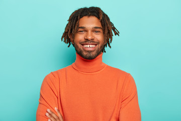 Positive emotions concept. Handsome dark skinned hipster with dreads has pleasant smile, has white...