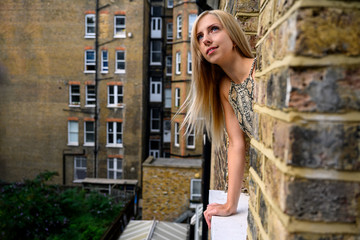 Portrait of young woman wistfully looking out of the window of an old brick building and hoping for better things to come in London, England