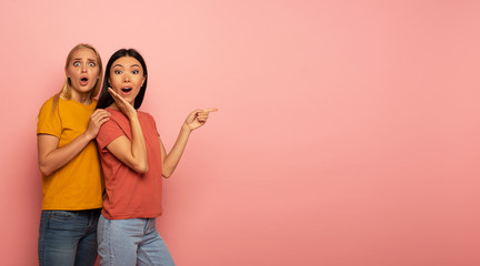Two girls indicates something. Amazed expression face. Pink background with blank space for your text