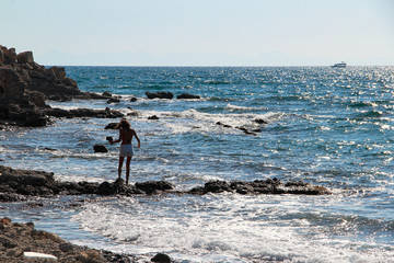 Woman alone at the rocky beach looking over the horizon with  wavy sea on a wind day in Mediterranean