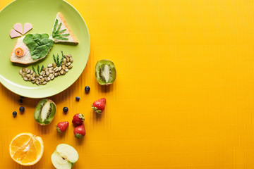 top view of plate with fancy fish made of food near fruits on colorful orange background