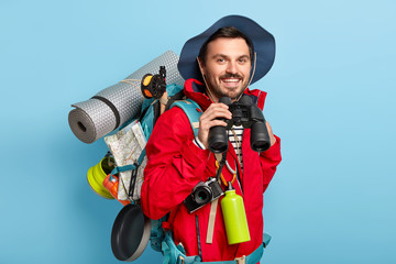 Traveler man has walk with backpack, carries necessary things for trip, looks through binoculars,...