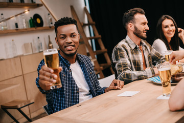 smiling african american man looking at camera while sitting in pub with multicultural friends