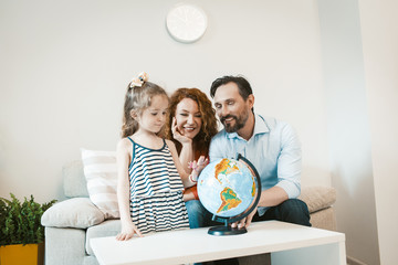 Going on adventure, mom, dad and daughter studying globe.
