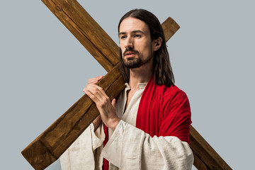 Obraz premium handsome bearded man in jesus robe holding wooden cross isolated on grey