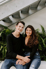 Fototapeta premium Cute Young Couple in Love Sitting in Front of Urban Concrete Stairs and Green Plants Cuddling, Kissing, and Holding Their Cold Brew Coffee Beverages