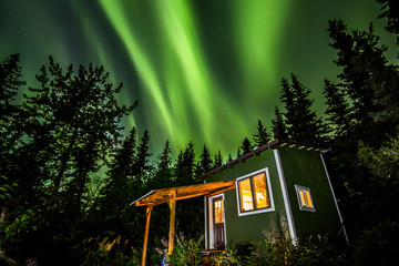 Bright green Aurora Borealis over small green and white tiny house in Alaska.