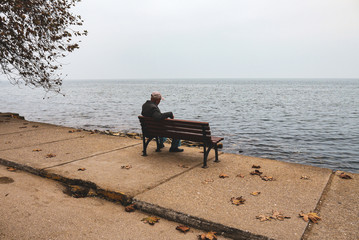 Naklejka na ściany i meble old man sitting at the bench looking to the horizon over the sea