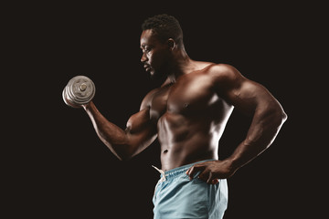 Fototapeta na wymiar Side view of african bodybuilder doing single arm dumbbell curl