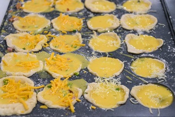 Individual quiches being made for breakfast, filled pastry shells in muffin tin ready to bake.