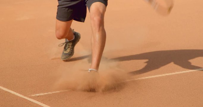 A tennis player slides into playing a shot on a clay tennis court in slow motion