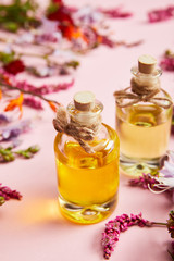 close up view of bottles with oil near fresh wild flowers on pink background