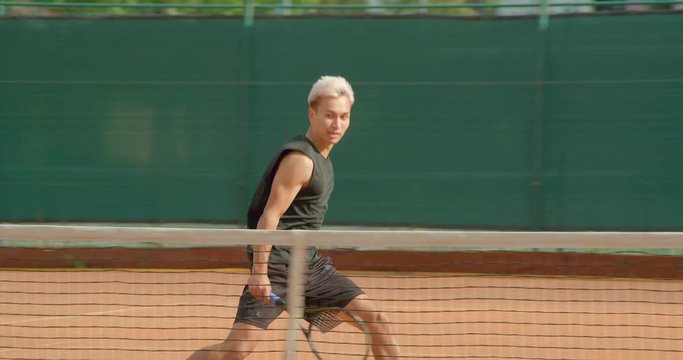 A Tennis player runs across the court at the net and volleys in slow motion.