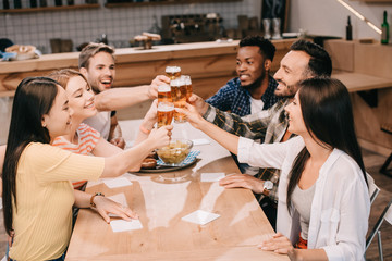 cheerful multicultural friends clinking glasses with beer while celebrating octoberfest in pub