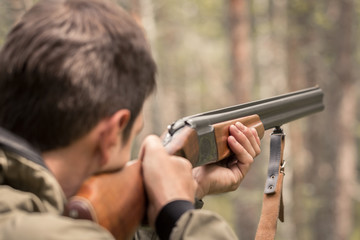 The hunter takes aim and is ready to shoot from a double barreled shotgun. Huntsman in the forest waiting for prey. Targeted rifle in the hands of a poacher.