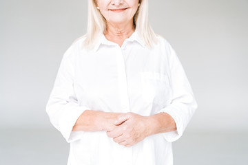 cropped view of happy blonde senior woman in white clothes isolated on grey