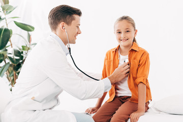 smiling pediatrist in white coat examining kid with stethoscope