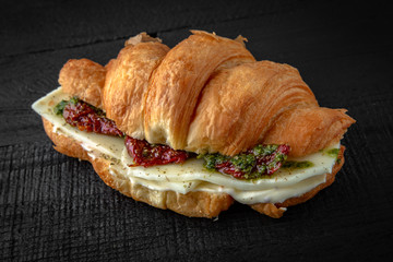 Vegetarian Croissant sandwich with mozzarella cheese, chedar, sun-dried tomatoes, pesto sauce. Healthy, tasty, nourishing snack. Take away food