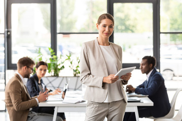 smiling beautiful businesswoman holding digital tablet in office