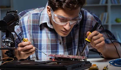 Young repair technician soldering electrical parts on motherboar