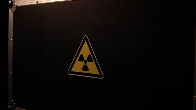 Radioactive (atomic ionizing radiation) danger warning symbol in triangular on a black case. Black suitcase with a sign of radiation hazard. Dark background.