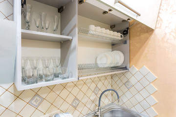 set of plates, cups and wine glasses on the shelf in the kitchen cabinet